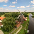 Mühle_Luftaufnahme.jpg Luftaufnahme einer historischen Mühle bei klarer Sicht, umgeben von grüner Landschaft und einem Fluss.