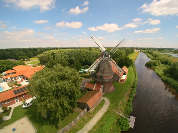 Mühle_Luftaufnahme.jpg Luftaufnahme einer historischen Mühle bei klarer Sicht, umgeben von grüner Landschaft und einem Fluss.