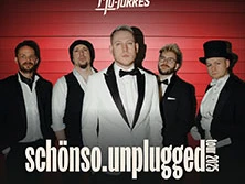 Fünf Musiker, elegant gekleidet in Schwarz-Weiß, stehen vor einer roten Wand und blicken entschlossen.