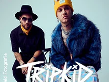 Zwei junge Männer in stylischer Kleidung und Accessoires posieren selbstbewusst vor einem neutralen Hintergrund.