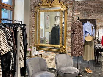 Simon und Renoldi Ein stilvolles Bekleidungsgeschäft mit zwei bequemen Sesseln, goldverziertem Spiegel und eleganter Kleidung auf Kleiderstangen.A stylish clothes store with two comfortable armchairs, a gold-decorated mirror and elegant clothes on clothes rails.