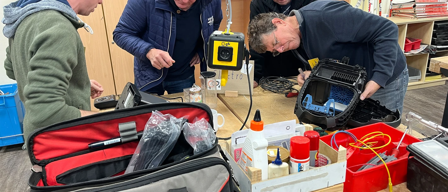 repair-cafe-bad-zwischenahn-elektrogeraete.jpg Four men concentrate on their work in a Repair Café. Tools and electronics lie on the table.