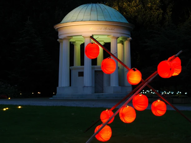 Nacht der 10000 Kerzen ©Staatsbad Salzuflen GmbH Beleuchteter Kurpark mit rotem Laternenvorhang und beleuchtetem Pavillon vor nächtlichem Himmel.