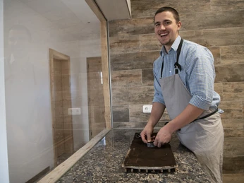 Seifenmanufaktur Wurm Ein Mann in Schürze lacht, während er in einer Werkstatt arbeitet.