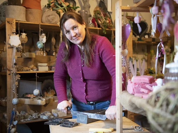 Seifenmanufaktur Wurm Seifenherstellerin arbeitet in ihrem Laden, umgeben von handgemachten Seifen und Dekorationen.