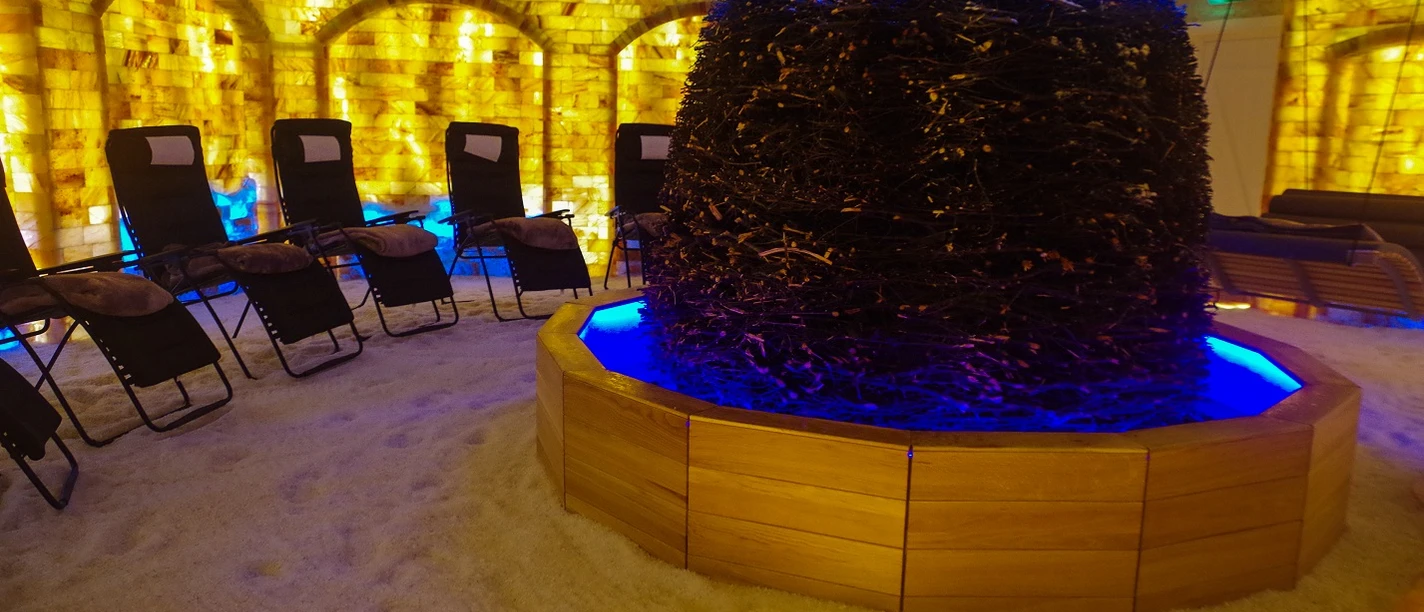 Salzgrotte Mehringer Heide-Ruheraum.jpg Ruheraum mit beleuchteten Salzwänden, Liegestühlen und Gradierwerk in warmem, beruhigendem Licht.