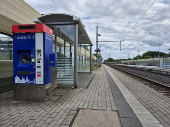 20250530_172521.jpg Moderner Bahnhof mit blauem Ticketautomaten, Bahnsteig, Gleisen und überdachter Wartezone