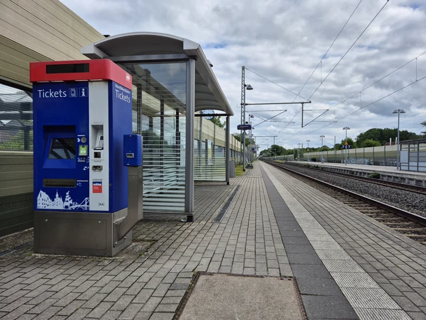 20250530_172521.jpg Moderner Bahnhof mit blauem Ticketautomaten, Bahnsteig, Gleisen und überdachter Wartezone