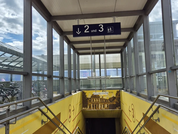 20250530_171119.jpg Überdachter Treppenabgang mit gelben Wänden zu den Bahnsteigen 2 und 3, mit Wegweisern und Handläufen.