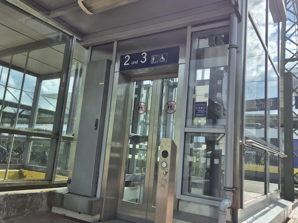20250530_171048.jpg Gläserner Aufzug am Bahnhof mit Bedientaster und barrierefreiem Zugang zu den Gleisen 2 und 3.