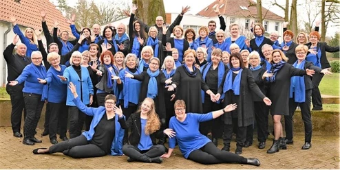 Kultur trifft Kirche Eine fröhliche Gruppe in blauen Outfit sitzt und steht draußen lachend zusammen, Bäume im Hintergrund.
