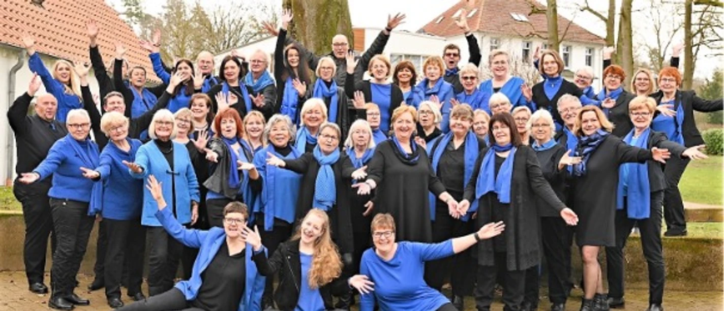 Kultur trifft Kirche Eine fröhliche Gruppe in blauen Outfit sitzt und steht draußen lachend zusammen, Bäume im Hintergrund.