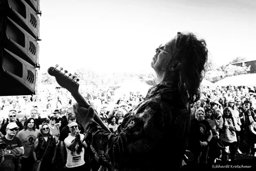 251018_ScottWeisBandSW.jpg Muzikant speelt elektrische gitaar voor een enthousiast publiek op een openluchtfestival.