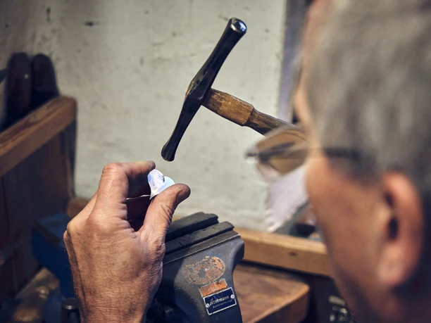 Silberschmied Adam bei der Arbeit Silberschmied arbeitet konzentriert mit Hammer und Amboss an einem Silberstück.