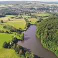 Nethestausee-Neuenheerse-2_SF_Bad-Driburger-Touristik-GmbH.png Luftaufnahme des Nethestausees, umgeben von dichten Wäldern und Feldern, Dorf im Hintergrund.