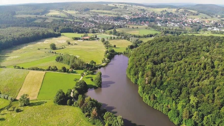 Nethestausee-Neuenheerse Luftaufnahme des Nethestausees, umgeben von dichten Wäldern und Feldern, Dorf im Hintergrund.