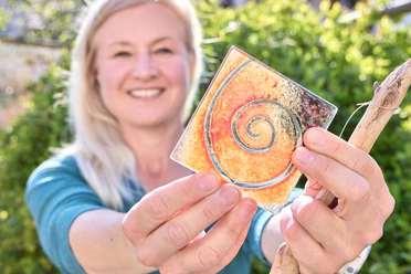 Sonnenberg Glas Eine Frau hält eine bunte, gläserne Kachel mit Spiralmuster in der Hand.