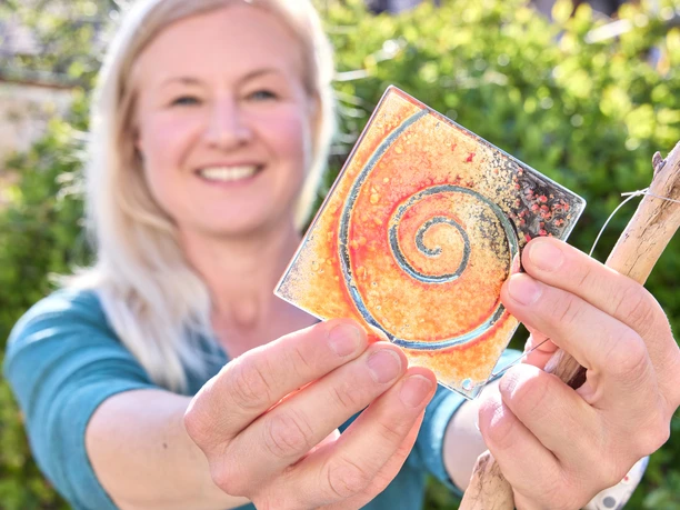 Sonnenberg Glas Eine Frau hält eine bunte, gläserne Kachel mit Spiralmuster in der Hand.