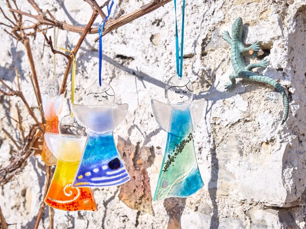 Glasengel Sonnenberg Glas Glasengel in verschiedenen Farben hängen an einer Wand, daneben eine kleine Eidechse.