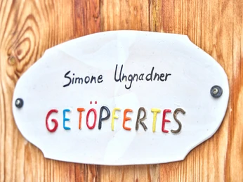 Ungnadner Keramik "Schild mit der Aufschrift 'Simone Ungnadner GETÖPFERTES' an Holzwand befestigt."