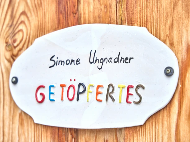 Ungnadner Keramik "Schild mit der Aufschrift 'Simone Ungnadner GETÖPFERTES' an Holzwand befestigt."
