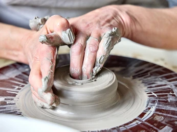 Ungnadner Keramik Hände formen Ton auf einer Drehscheibe, konzentriert auf präzise Verarbeitung.
