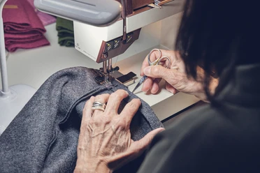 Wuide Henna beim Nähen Nähen an einer Maschine mit grauem Stoff in einem Handwerksbetrieb.