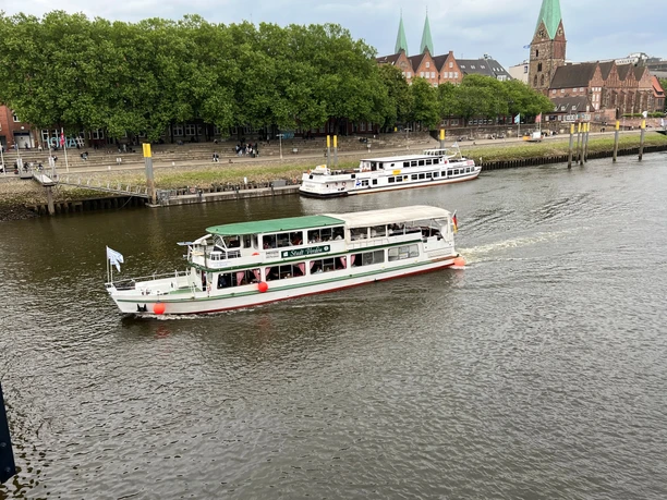 Een wit passagiersschip vaart op de Weser in Bremen, met een groen landschap op de achtergrond.