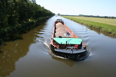 Schleusenkanal Balge Een vrachtschip glijdt over een rustig kanaal, omringd door groene bomen en open velden.