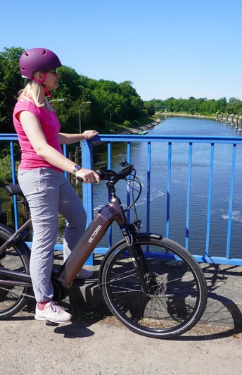 Eine Radfahrerin steht auf einer blauen Brücke und blickt auf den Schleusenkanal Balge.