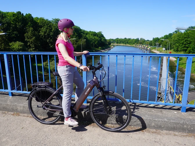 Schleusenkanal Balge Eine Radfahrerin steht auf einer blauen Brücke und blickt auf den Schleusenkanal Balge.A cyclist stands on a blue bridge and looks out over the Balge lock canal.En cyklist står på en blå bro og kigger ud over slusekanalen i Balge.Een fietser staat op een blauwe brug en kijkt uit over het kanaal van de Balge-sluis.