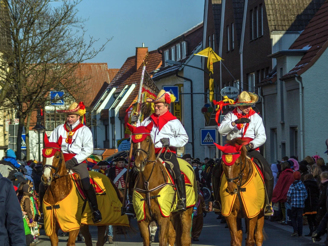 Karneval ©Stadt Delbrück Karnevalsumzug in Delbrück mit verkleideten Reitern auf Pferden in einer belebten Straße.