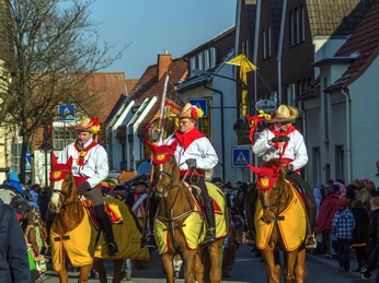 Karneval ©Stadt Delbrück Karnevalsumzug in Delbrück mit verkleideten Reitern auf Pferden in einer belebten Straße.