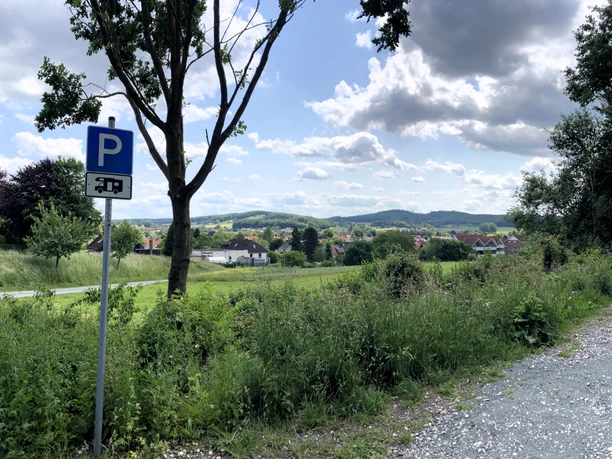 Landschaftliche Ausblick mit Wohnmobilstellplatzschild, grünen Feldern und malerischen Hügeln.