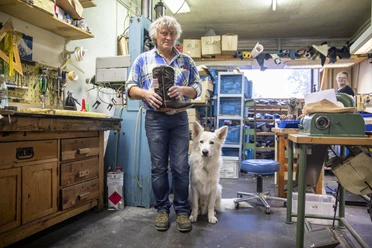 Schuhmacherei Zollner Schuhmacher und weißer Hund in einer Werkstatt voller Werkzeug und Maschinen.