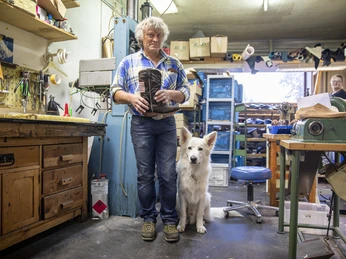 Schuhmacherei Zollner Schuhmacher und weißer Hund in einer Werkstatt voller Werkzeug und Maschinen.