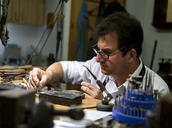 Goldschmied Thomas Schwabe Goldschmied bei der Arbeit an einem Werkbank mit Werkzeugen und Materialien.