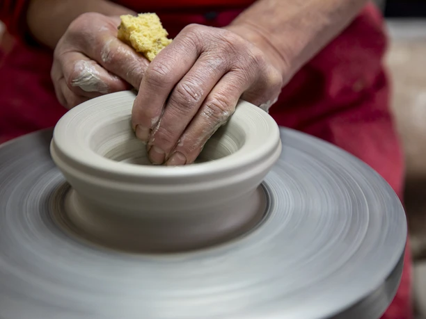 Töpferei Winsi Hände formen Ton auf einer rotierenden Töpferscheibe mit einem Schwamm.