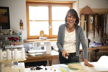 Barbara Raggl Eine Frau in einer Werkstatt schneidet Stoff mit einem Rollschneider zu.