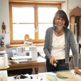Barbara Raggl Eine Frau in einer Werkstatt schneidet Stoff mit einem Rollschneider zu.