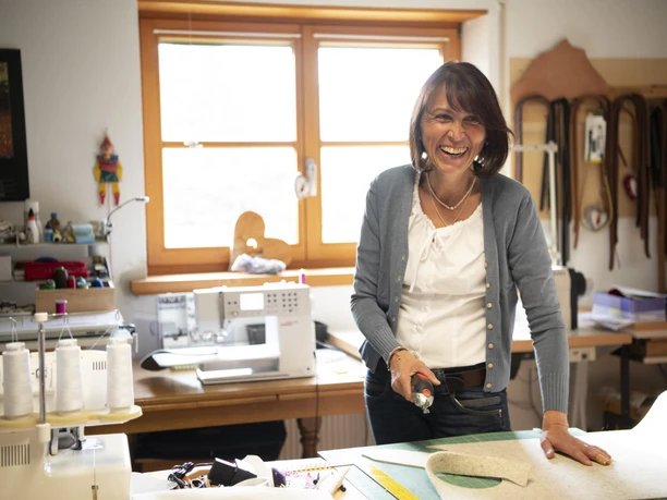 Barbara Raggl Eine Frau in einer Werkstatt schneidet Stoff mit einem Rollschneider zu.