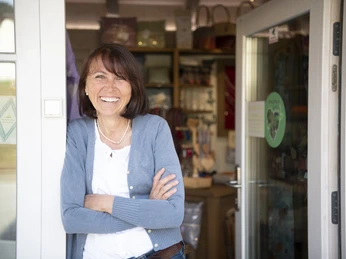 Barbara Raggl Geschäftsfrau lächelt im Eingangsbereich eines Handwerksladens, typisch einladend.