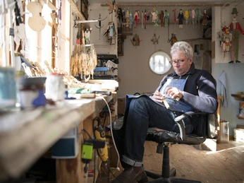 Oberammergauer Schnürlkasperl Ein Handwerker schnitzt konzentriert in einer Werkstatt an einer Holzfigur.