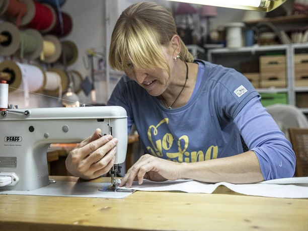 Nöh´s Raumausstattung Handwerkerin näht konzentriert an einer Nähmaschine in einer Werkstattumgebung.