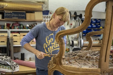Nöh´s Raumausstattung Person bei der Restaurierung eines Holzsessels mit Drahtfedern in einer Werkstatt.