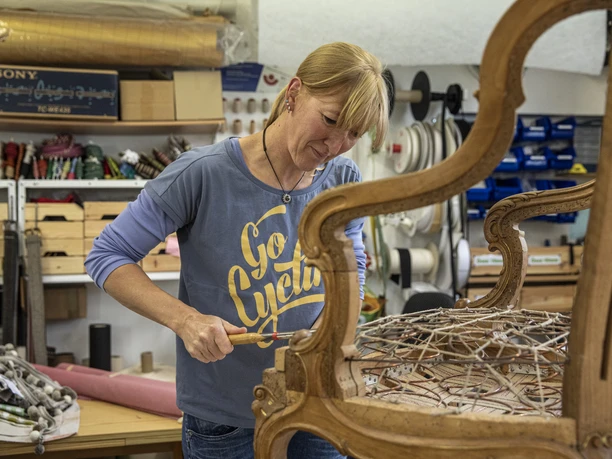 Nöh´s Raumausstattung Person bei der Restaurierung eines Holzsessels mit Drahtfedern in einer Werkstatt.