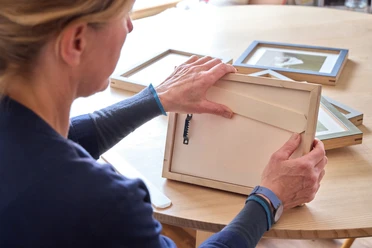 naïndesign Person prüft einen Holz-Bilderrahmen an einem Tisch mit anderen Rahmen.