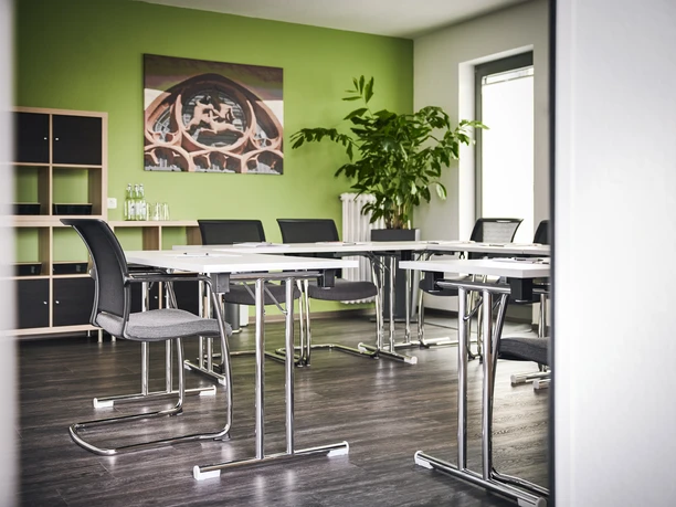 In Via Hotel Heller Seminarraum mit moderner Einrichtung: Tischgruppen, graue Stühle und grüne Wandgestaltung.