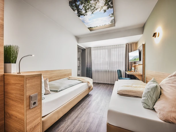 Modernes Hotelzimmer mit zwei Einzelbetten, großem Fenster, wandmontiertem Fernseher und natürlichem Licht.