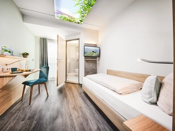 In Via Hotel Modern eingerichtetes Hotelzimmer mit Einzelbett, Schreibtisch und Badezimmer im Hintergrund.